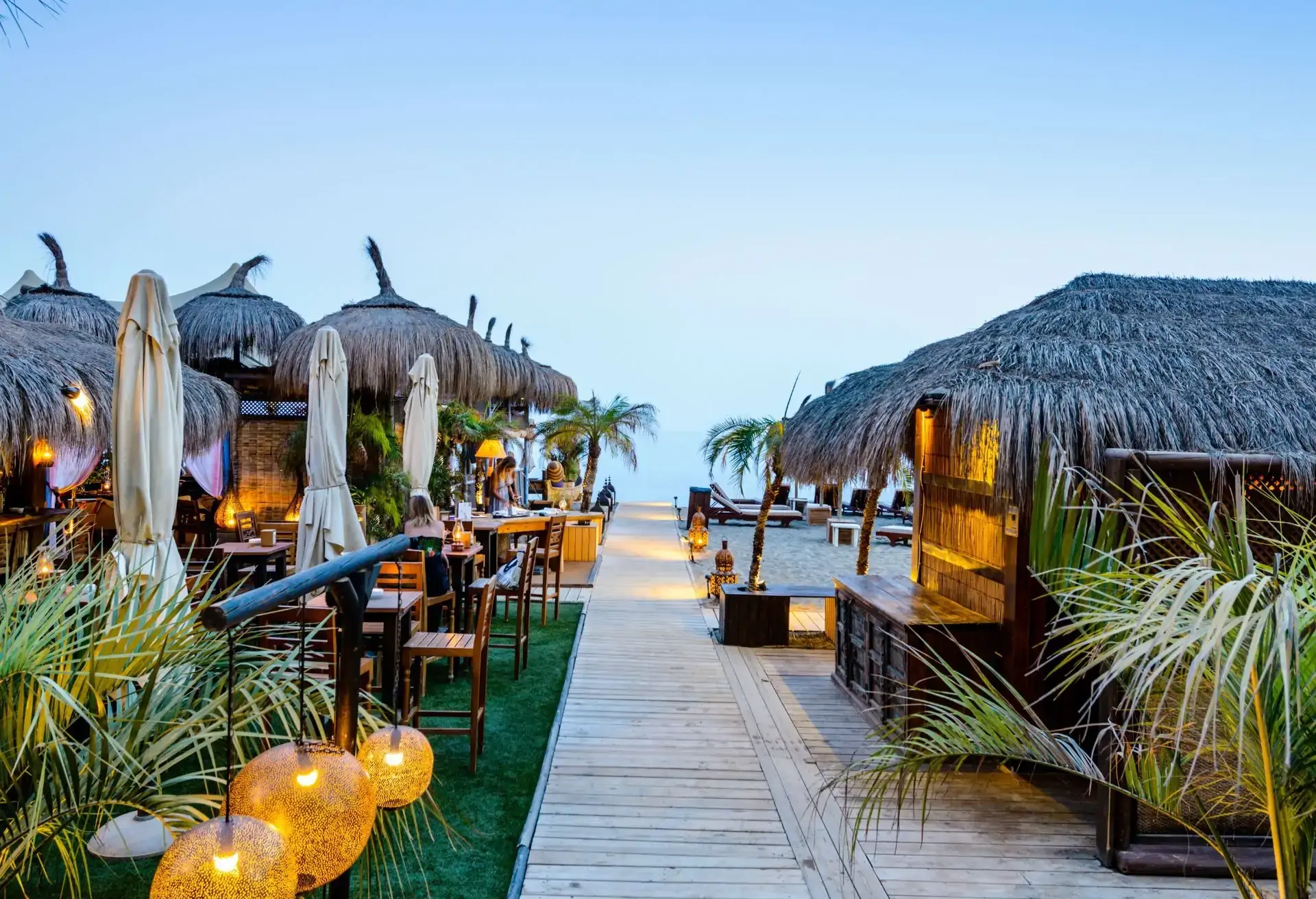 Tropical beachside restaurant with thatched huts and cozy evening lighting.