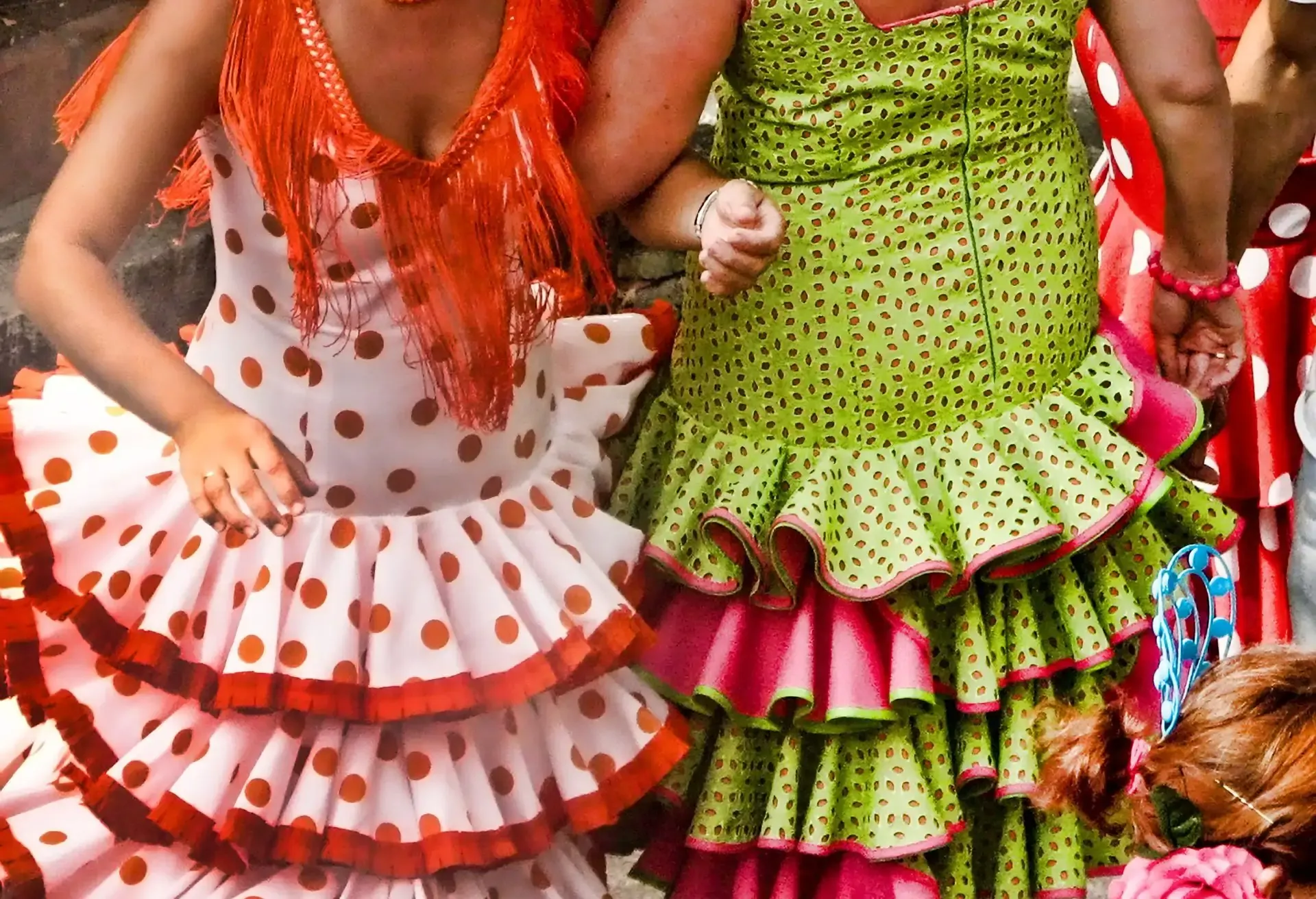 Women wearing colorful flamenco dresses with polka dots and ruffled skirts.