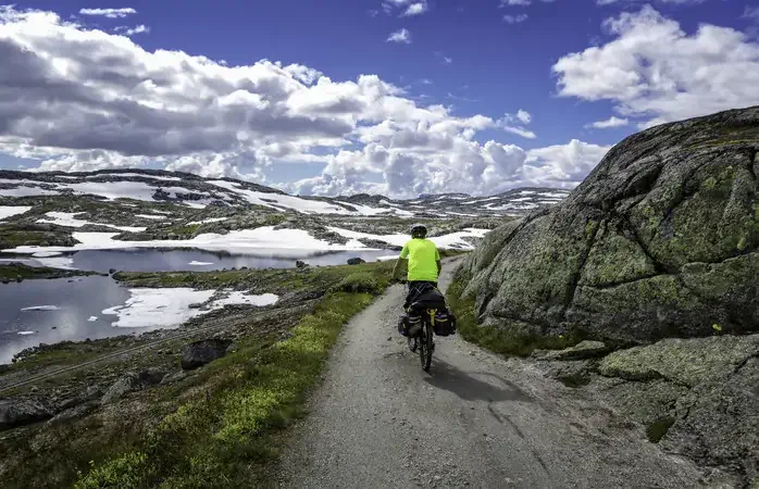 Norway, summer 2014. Young man bicycles Rallarvegen, that runs between Haugastøl and Flåm. Hardangervidda National Park. Beautiful scenery with small lakes and high mountains. Sunny and warm, but still a little snow.