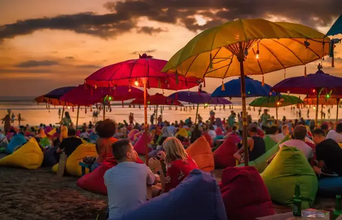 Denpasar, Bali, Indonesia - 17 June 2018: Tourists relaxing and sitting on colorful bean bags, under the umbrellas, and enjoying the sunset at the beach.